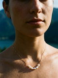 Close-up of a person wearing a necklace with a blurred natural background, Modern freshwater pearl pendant necklace with delicate gold chain - everyday luxury jewelry by Ozey